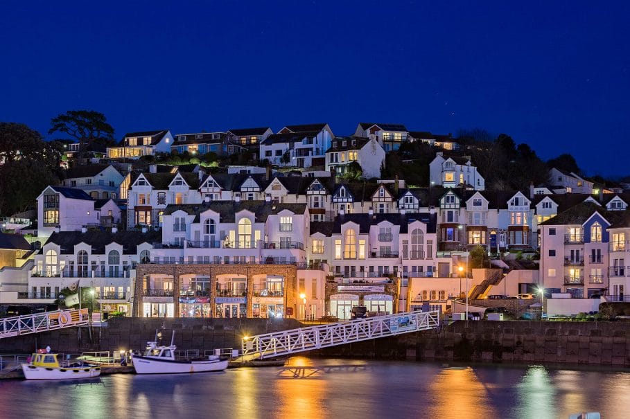 Brixham Harbour at night, lit up by street lights and lights from the houses.