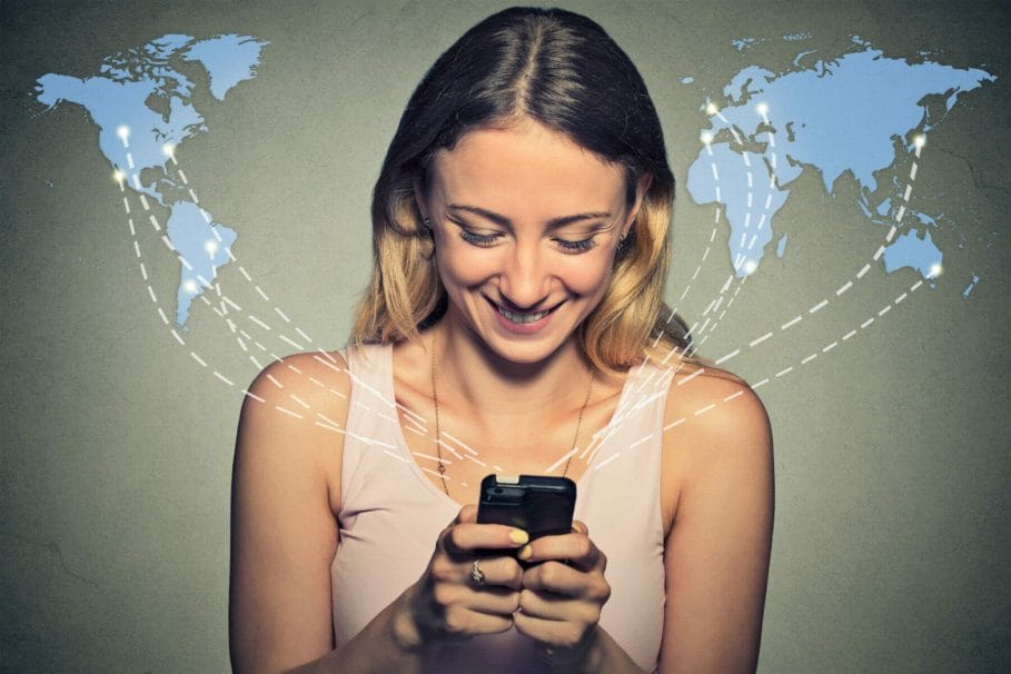 Woman using smart phone, while smiling against a background that shows a world map