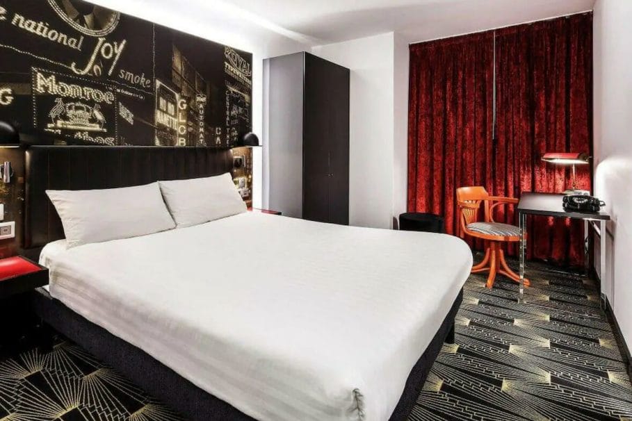 Double room inside the ibis styles hotel in Stylewalk, London. The room has a theatre theme to it with red curtains and a black wall that has theatre signs printed on it.
