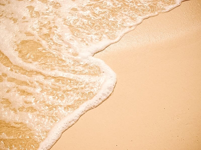 photo of golden sand with sea foam left behind, after a wave has come in and gone back out.