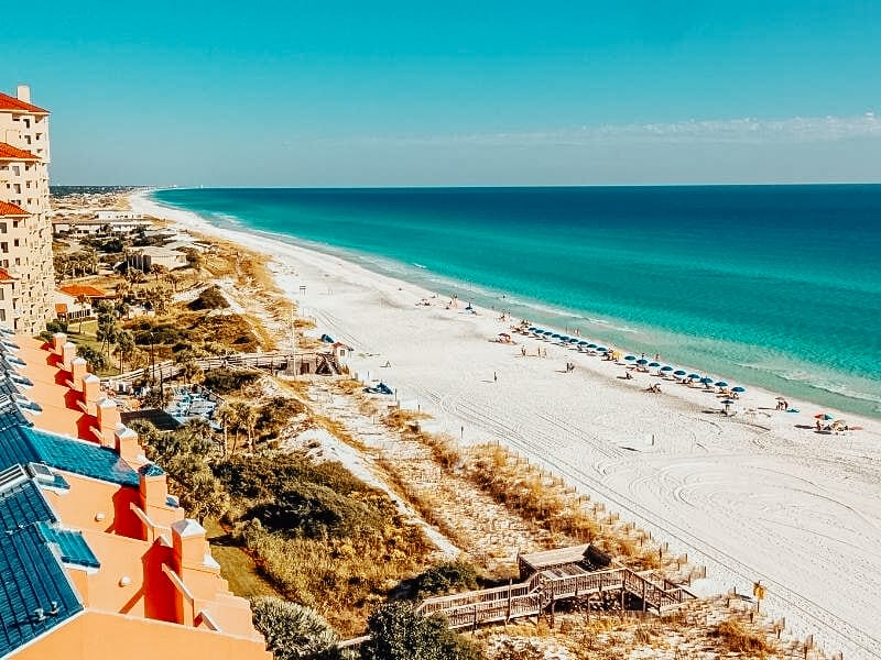 View over Miramar Beach, showing the emerald green waters and white sandy beach with deckchairs and umbrellas. 