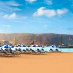 Sunloungers and umbrellas on los Cristianos beach with a pirate style ship in the waters