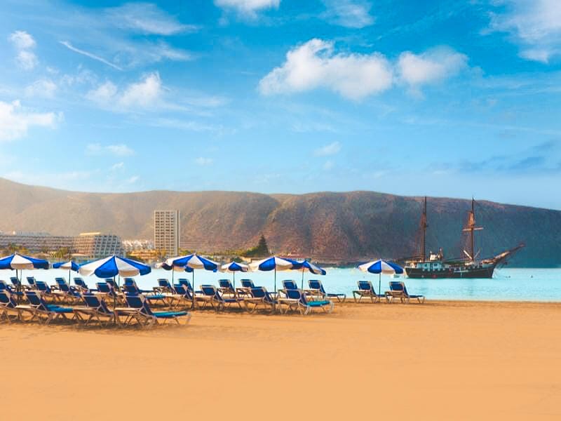 Sunloungers and umbrellas on los Cristianos beach with a pirate style ship in the waters