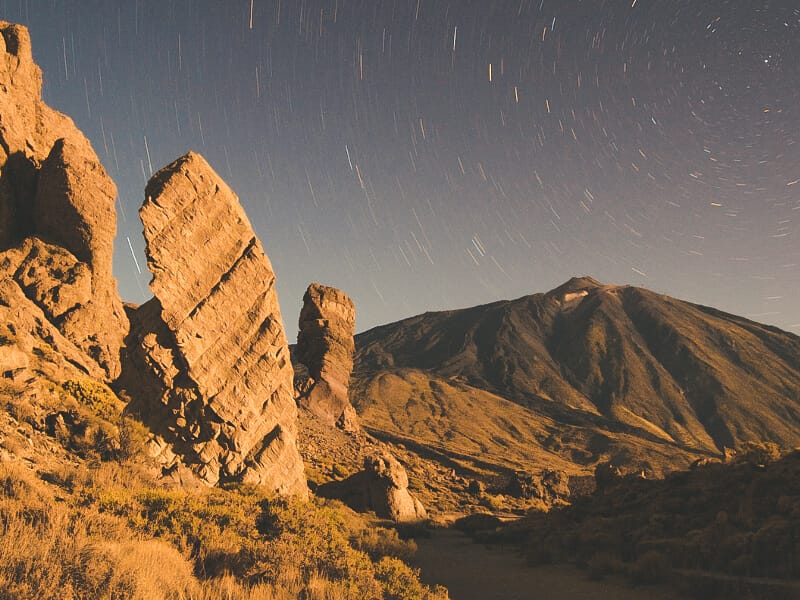 Mount teide at night, with a starry sky and rock formations in front of the mountani