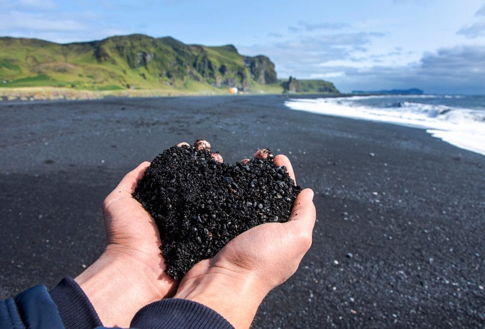 Hand sholding black sand in a shape of a heart