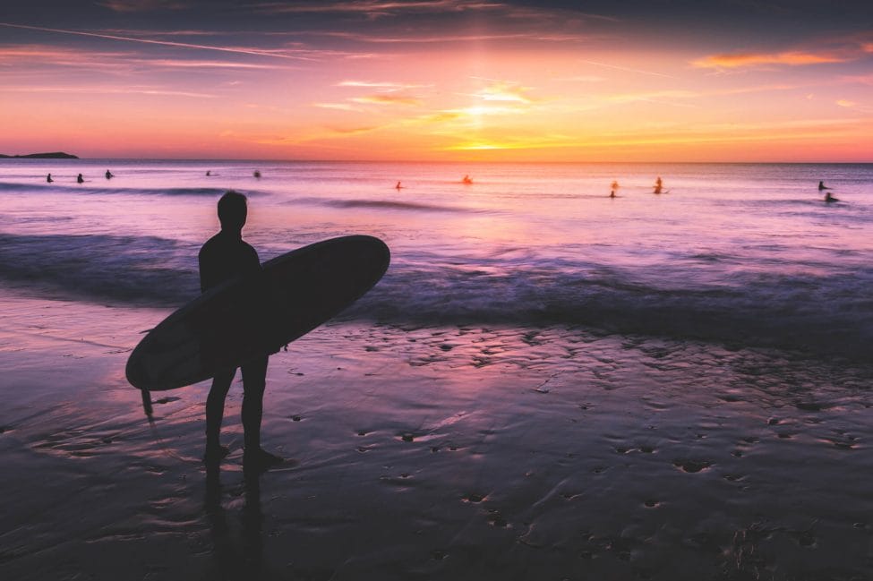 Surfer on beach at sunset in Cornwall, England