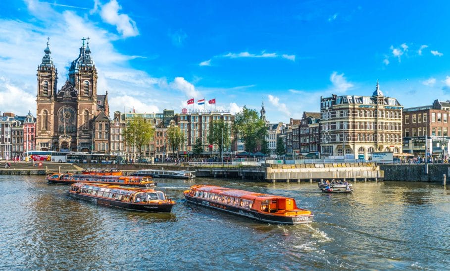 Photo of 3 lover canal boats in front of Amsterdam Central Station, where they come in to moor so passengers can get on/off.