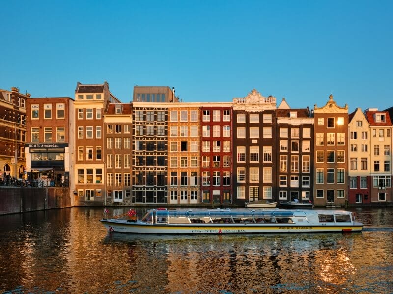 Closed top Stromma canal boat cruising along the Amsterdam canal during sunset.