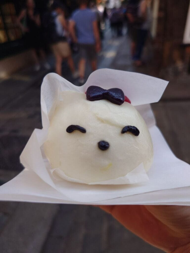 A picture of a custard boa from Meow and Bao in York. The bao is white, with a cute face and a hair bow. 