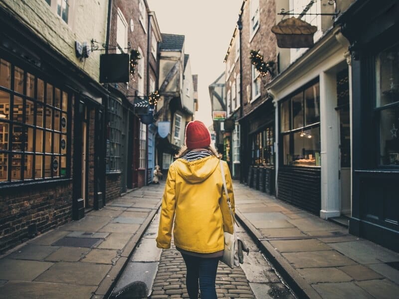 Solo woman wiht a yellow coat and red hat walking down the shambles in York