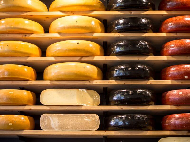 Gouda cheese wrapped and stacked on wooden shelves in a cheese shop