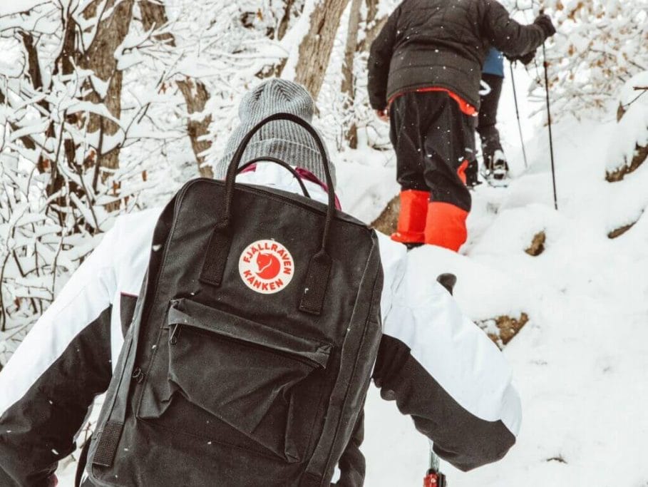 person in black jacket and red pants carrying black backpack on snow covered ground during daytime