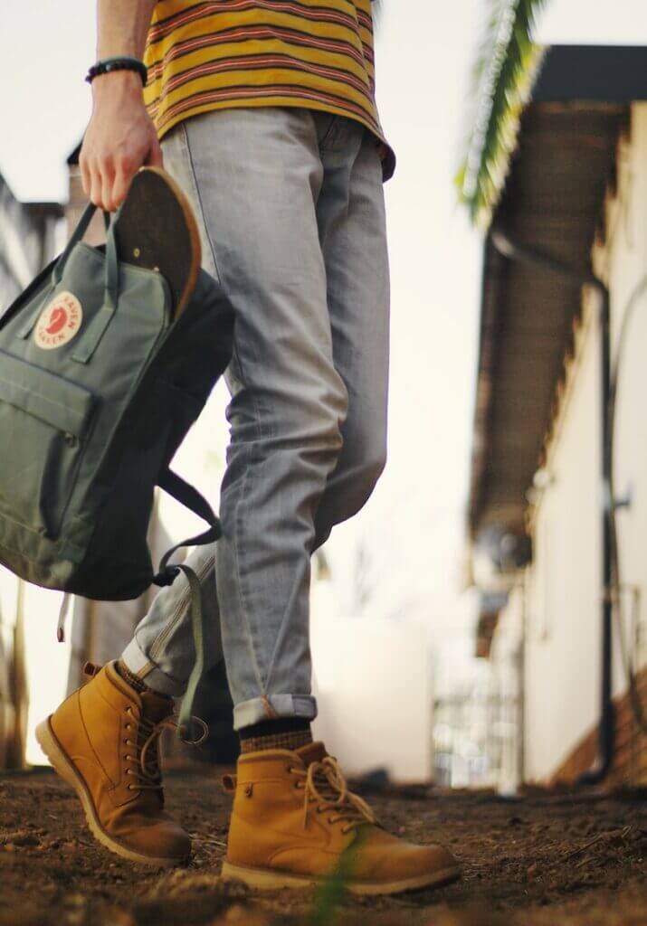person in blue denim jeans and brown leather boots with a fjallraven backpack
